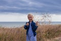 Adorable little girl in denim jacket back view on a hill with sea landscape view. Stylish child long blond hair faceless