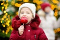 Adorable little girl eating red apple covered with sugar icing on traditional Christmas market. Royalty Free Stock Photo
