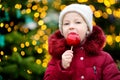 Adorable little girl eating red apple covered with sugar icing on traditional Christmas market. Royalty Free Stock Photo