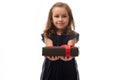 Adorable little girl in evening dark blue dress holding a black gift box with red ribbon on her hands and showing it to camera. Royalty Free Stock Photo