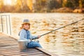 Adorable little girl fishing with fishing rod at the pond at the sunset