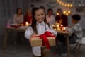 Adorable little girl giving wrapped gift box at camera during festive dinner at home, selective focus Royalty Free Stock Photo