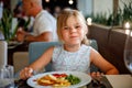 Adorable little girl having breakfast at resort restaurant. Happy preschool child eating healthy food, vegetables and Royalty Free Stock Photo