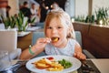 Adorable little girl having breakfast at resort restaurant. Happy preschool child eating healthy food, vegetables and Royalty Free Stock Photo