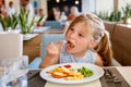 Adorable little girl having breakfast at resort restaurant. Happy preschool child eating healthy food, vegetables and Royalty Free Stock Photo