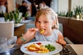 Adorable little girl having breakfast at resort restaurant. Happy preschool child eating healthy food, vegetables and Royalty Free Stock Photo