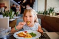 Adorable little girl having breakfast at resort restaurant. Happy preschool child eating healthy food, vegetables and Royalty Free Stock Photo