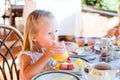 Adorable little girl having breakfast at restaurant. Cute kid enjoy fresh orange juice in outdoor cafe Royalty Free Stock Photo