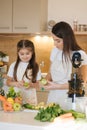 Adorable little girl helping her mom to make fresh juice at home. Two females in apron. Fruits and vegetables. Homemade Royalty Free Stock Photo