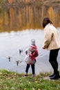 Adorable little girl and her mother feed ducks in the river. Leisure with children.