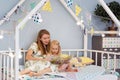 Adorable little girl and her young mother are reading a book and smiling while sitting in decorated house bed Royalty Free Stock Photo