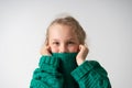 Adorable little girl hiding lower part of her face under thick collar of warm knitted sweater. Close up studio shot Royalty Free Stock Photo