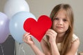 Adorable little girl holding big red heart near air balloons. Valentines Day, love, mothers fathers Day, romantic