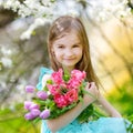 Adorable little girl holding tulips for her mother in blooming cherry garden Royalty Free Stock Photo