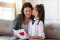 Adorable little girl kissing mommy, presenting handmade card.