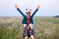 Adorable little girl with long braided hair in plaid skirt on hill with raised hands up to the sky. Happy traveler child