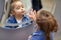 Adorable little girl making faces and looking at herself in the mirror, touching a button on a mirror, luminous mirror Royalty Free Stock Photo