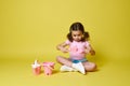 Adorable little girl playing with shovel and rake, sitting near a set of beach toys. Isolated summer concepts on yellow background Royalty Free Stock Photo