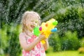 Adorable little girl playing with water gun on hot summer day. Cute child having fun with water outdoors. Royalty Free Stock Photo