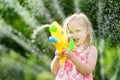 Adorable little girl playing with water gun on hot summer day. Cute child having fun with water outdoors. Royalty Free Stock Photo