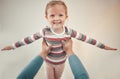 Adorable little girl pretending to fly with arms outstretched while being lifted in the air by parent. Cute kid having