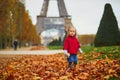 Adorable little girl in red poncho walking inear the Eiffel tower on a fall day