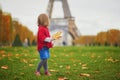 Adorable little girl in red poncho walking inear the Eiffel tower on a fall day