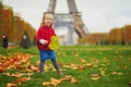 Adorable little girl in red poncho walking inear the Eiffel tower on a fall day