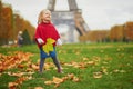 Adorable little girl in red poncho walking inear the Eiffel tower on a fall day