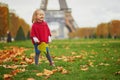 Adorable little girl in red poncho walking inear the Eiffel tower on a fall day