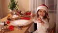 Adorable little girl in red santa hat dancind by the table. Preparing for Christmas at home. Baking gingerbread