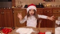 Adorable little girl in red santa hat dancind by the table. Preparing for Christmas at home. Baking gingerbread