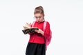 Adorable little girl in red school jacket, black dress, backpack and rounded glasses surprized or amazed looking at book