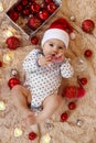 Adorable little girl in Santa Claus red hat is playing with wooden toy on a beige plaid with red and white Christmas decorations. Royalty Free Stock Photo