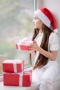 Pretty little girl in Santa hat dreaming by the window holding g Royalty Free Stock Photo