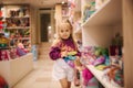 Adorable little girl shopping for toys. Cute female in toy store. Happy young girl selecting toy