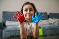 Adorable little girl showing her hands painted in red and blue paints, cutely smiles to the camera. Creative hobby Royalty Free Stock Photo