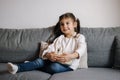 Adorable little girl sits on sofa and watching TV at home. Cute girl eating popcorn. Holiday mood Royalty Free Stock Photo