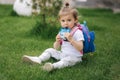 Adorable little girl sitting on the grass with backpack. Cute little girl drinking juise outdoors