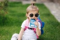 Adorable little girl sitting on the grass with backpack. Cute little girl drinking juise outdoors