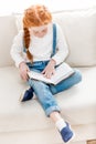 Adorable little girl sitting on sofa and reading book Royalty Free Stock Photo