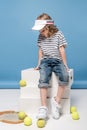 adorable little girl sitting on white boxes and looking at tennis raquet