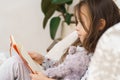 Adorable little girl in sleepwear lying on couch and reading book. Portrait of child, preschooler, side view.