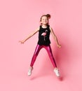 Adorable little girl in sleeveless t-shirt with flamingo and bright rose leggings is merrily jumping on place.