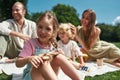 Adorable little girl smiling at camera while relaxing with parents and brother outdoors, having picnic in nature on a Royalty Free Stock Photo