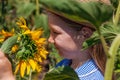 Adorable little girl in straw hat, blue plaid summer dress in a field countryside. Child with long hair smells sunflower Royalty Free Stock Photo