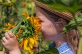 Adorable little girl in straw hat, blue plaid summer dress in a field countryside. Child with long hair smells sunflower Royalty Free Stock Photo