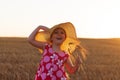 Adorable little girl in a straw hat and pink summer dress in wheat field. Child with long blonde hair on sunset, farming Royalty Free Stock Photo