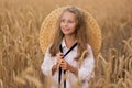 Adorable little girl in a straw hat in wheat field. Child with long blonde wavy hair on countryside landscape with spikelet in Royalty Free Stock Photo