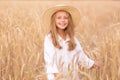 Adorable little girl in a straw hat in wheat field. Child with long blonde wavy hair on countryside landscape with spikelet in Royalty Free Stock Photo